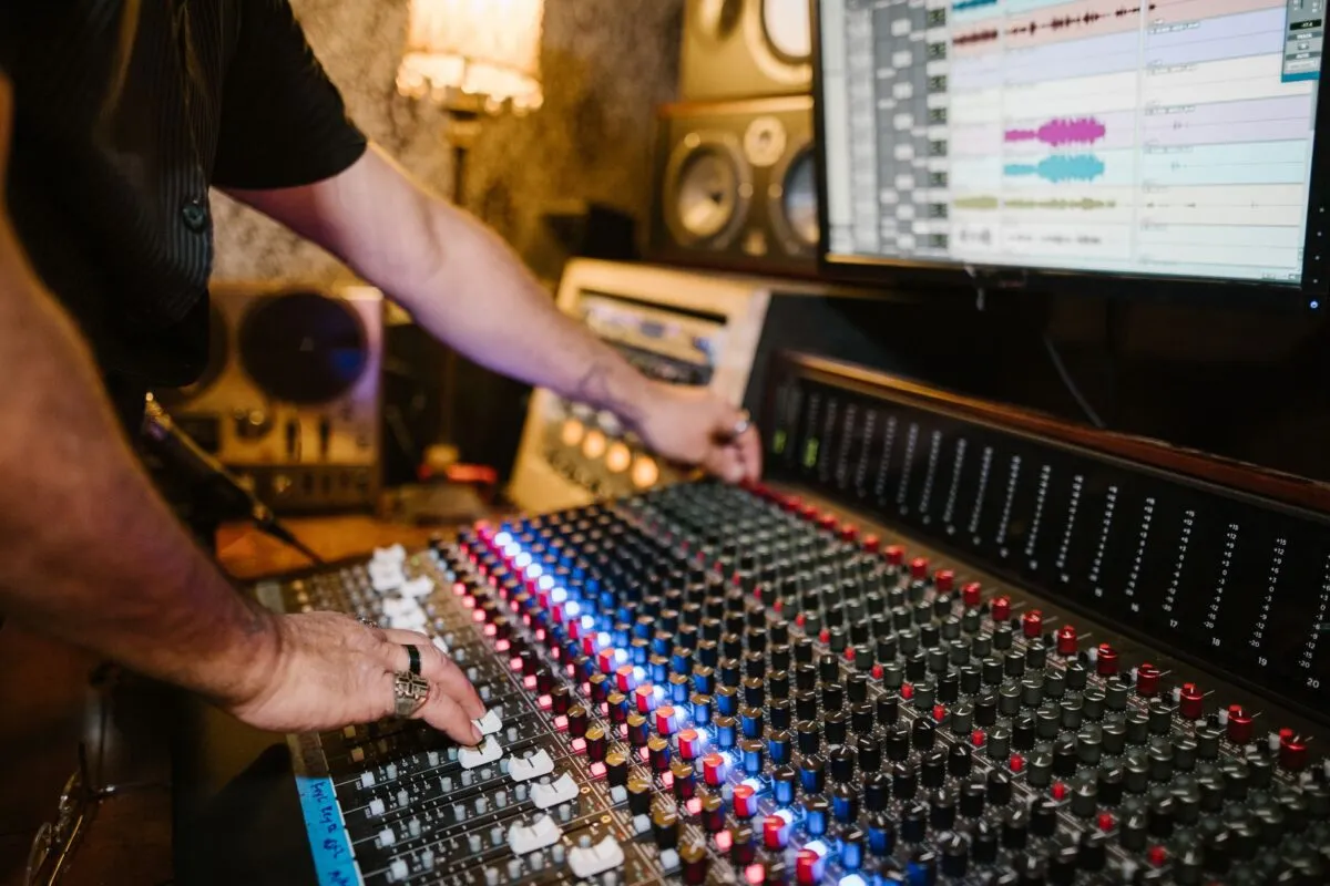 Como a inteligência artificial está mudando a música Mãos de um produtor operando mesa de mixagem em estúdio de gravação com tela de áudio digital
