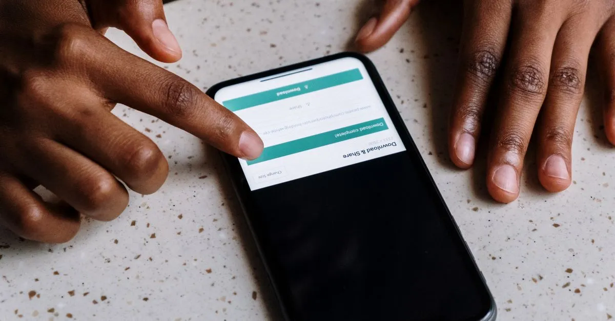Como baixar app de apostas com segurança Mãos de uma pessoa tocando um smartphone exibindo uma tela interativa.